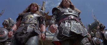 Movie still from “Conan the Barbarian” (1982), directed by John Milius – A couple of men dressed in armor and holding hands; Medium shot, Low angle