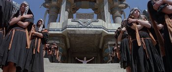 Movie still from “Conan the Barbarian” (1982), directed by John Milius – A man standing on top of a staircase in front of a group of people; Extreme Wide shot, Low angle