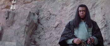 Movie still from “Conan the Barbarian” (1982), directed by John Milius – A woman in a black and white outfit standing in front of a rock wall; Close Up shot, Low angle