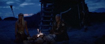 Movie still from “Conan the Barbarian” (1982), directed by John Milius – A man sitting in front of a fire at night; Wide shot, High angle