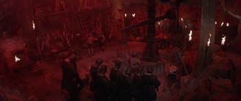Movie still from “Conan the Barbarian” (1982), directed by John Milius – A group of people standing in a room with red lighting; Extreme Wide shot, High angle