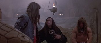 Movie still from “Conan the Barbarian” (1982), directed by John Milius – A man with long black hair talking to another man; Medium shot, Over the shoulder angle