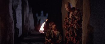 Movie still from “Conan the Barbarian” (1982), directed by John Milius – A man and a woman are standing next to a fire; Medium shot, Over the shoulder angle