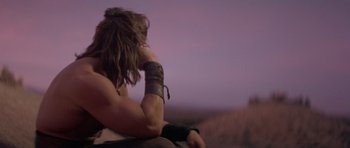 Movie still from “Conan the Barbarian” (1982), directed by John Milius – A man sitting on top of a hill with his hand on his chin; Medium shot, Over the shoulder angle