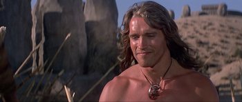 Movie still from “Conan the Barbarian” (1982), directed by John Milius – A person with long hair wearing a necklace; Close Up shot, Over the shoulder angle