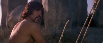 Movie still from “Conan the Barbarian” (1982), directed by John Milius – A man with long hair is holding a bow and arrow; Close Up shot, Over the shoulder angle