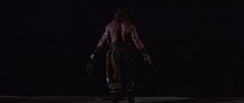 Movie still from “Conan the Barbarian” (1982), directed by John Milius – A man with no shirt is standing in the dark; Wide shot, Low angle