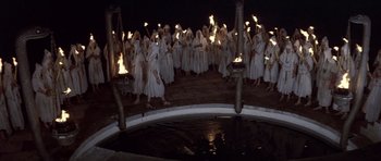 Movie still from “Conan the Barbarian” (1982), directed by John Milius – A group of people dressed in white holding torches in front of a pool; Wide shot, High angle