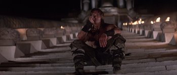 Movie still from “Conan the Barbarian” (1982), directed by John Milius – A man sitting on some steps in the dark; Medium shot, Low angle