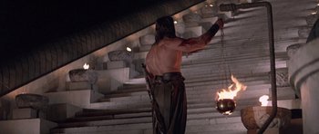 Movie still from “Conan the Barbarian” (1982), directed by John Milius – A man with a sword and a lantern on a staircase; Wide shot, Low angle