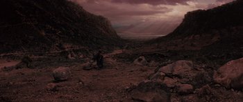 Movie still from “Conan the Barbarian” (1982), directed by John Milius – A person standing on a dirt path in the middle of a valley; Extreme Wide shot, High angle