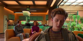 Movie still from “Big Bug” (2022), directed by Jean-Pierre Jeunet – A man and a woman sitting in a room with other people; Medium shot, Over the shoulder angle