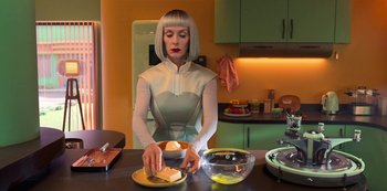 Movie still from “Big Bug” (2022), directed by Jean-Pierre Jeunet – A woman in a kitchen preparing food on a plate; Medium shot, Low angle