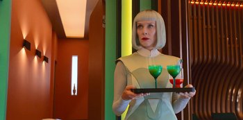 Movie still from “Big Bug” (2022), directed by Jean-Pierre Jeunet – A woman holding a tray with two glasses on top of it; Medium shot, Low angle