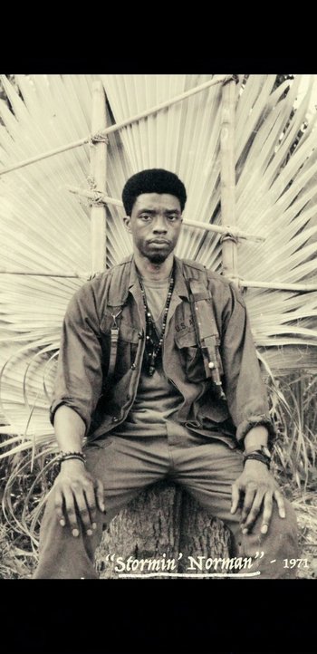 Movie still from “Da 5 Bloods” (2020), directed by Spike Lee – A black and white photo of a man sitting in a field; Close Up shot, Low angle
