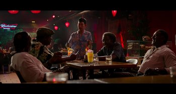Movie still from “Da 5 Bloods” (2020), directed by Spike Lee – A group of people sitting at a table with drinks; Wide shot, Over the shoulder angle