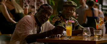 Movie still from “Da 5 Bloods” (2020), directed by Spike Lee – Two older men sitting at a table with a drink; Medium shot, Over the shoulder angle