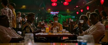 Movie still from “Da 5 Bloods” (2020), directed by Spike Lee – A group of people sitting at a table with drinks; Medium shot, Low angle