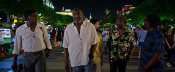 Movie still from “Da 5 Bloods” (2020), directed by Spike Lee – A group of people standing on a sidewalk at night; Medium shot, Over the shoulder angle