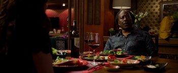 Movie still from “Da 5 Bloods” (2020), directed by Spike Lee – A man sitting at a table with a glass of red wine; Medium shot, Over the shoulder angle