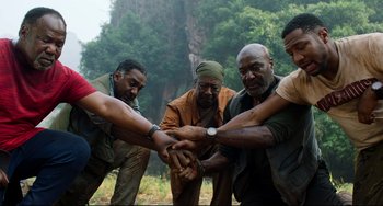 Movie still from “Da 5 Bloods” (2020), directed by Spike Lee – A group of men holding hands on a field; Medium shot, Low angle
