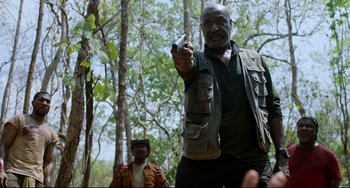 Movie still from “Da 5 Bloods” (2020), directed by Spike Lee – A man holding a gun while standing next to another man in the woods; Medium shot, Low angle