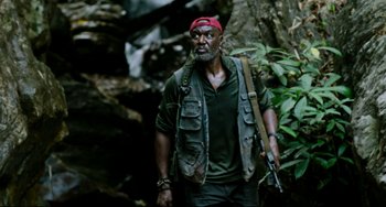 Movie still from “Da 5 Bloods” (2020), directed by Spike Lee – A man with a gun in his hand and a red hat; Medium shot, Low angle