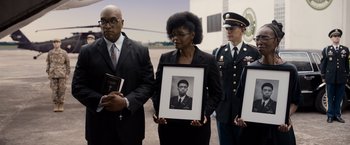 Movie still from “Da 5 Bloods” (2020), directed by Spike Lee – A woman holding a framed photo standing next to two men; Medium shot, Low angle