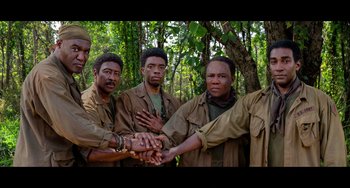 Movie still from “Da 5 Bloods” (2020), directed by Spike Lee – A group of men holding hands in a forest; Medium shot, Low angle