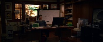 Movie still from “Bird Box” (2018), directed by Susanne Bier – A man sitting at a computer desk in front of a whiteboard; Wide shot, High angle