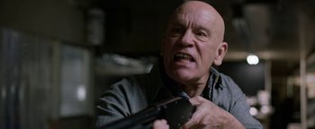 Movie still from “Bird Box” (2018), directed by Susanne Bier – An older bald man holding a gun in his hand; Close Up shot, Low angle