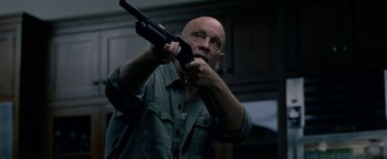 Movie still from “Bird Box” (2018), directed by Susanne Bier – A bald man holding a gun in his hands; Medium shot, Low angle