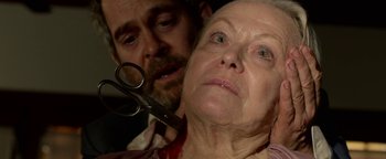 Movie still from “Bird Box” (2018), directed by Susanne Bier – An older woman is holding a pair of scissors in front of a younger man; Close Up shot, Over the shoulder angle