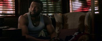 Movie still from “Bird Box” (2018), directed by Susanne Bier – A man sitting on top of a couch in front of a window; Medium shot, Over the shoulder angle