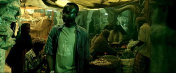 Movie still from “Black Hawk Down” (2001), directed by Ridley Scott – A man standing next to a bunch of vegetables; Medium shot, High angle