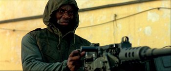 Movie still from “Black Hawk Down” (2001), directed by Ridley Scott – A man wearing a green jacket and a hood is holding a machine gun; Close Up shot, Low angle