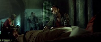 Movie still from “Black Hawk Down” (2001), directed by Ridley Scott – A man sitting on a bed smoking a cigarette; Medium shot, Over the shoulder angle