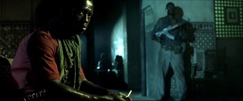 Movie still from “Black Hawk Down” (2001), directed by Ridley Scott – A man sitting in a dark room holding a cigarette in his hand; Medium shot, Over the shoulder angle