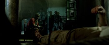 Movie still from “Black Hawk Down” (2001), directed by Ridley Scott – A group of men standing around a person laying on a bed; Wide shot, Low angle
