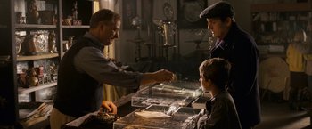 Movie still from “Dear John” (2010), directed by Lasse Hallström – A man handing a coin to a young boy in front of a glass case; Medium shot, Over the shoulder angle