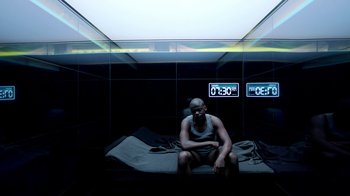 Movie still from “Black Mirror” (2011), created by Charlie Brooker – A man sitting on a bed in a dark room; Wide shot, High angle