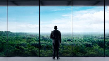 Movie still from “Black Mirror” (2011), created by Charlie Brooker – A man standing in front of a window looking out at a forest; Extreme Wide shot, Low angle