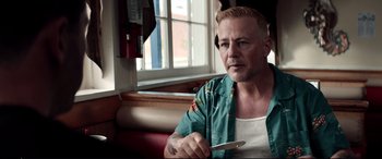 Movie still from “Debt Collectors” (2020), directed by Jesse V. Johnson – A man sitting at a table with a knife in his hand; Close Up shot, Over the shoulder angle