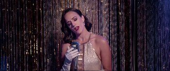 Movie still from “Debt Collectors” (2020), directed by Jesse V. Johnson – A woman in a gold dress holding a microphone; Medium shot, Low angle