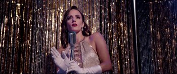 Movie still from “Debt Collectors” (2020), directed by Jesse V. Johnson – A woman holding a microphone in front of a microphone stand; Medium shot, Low angle