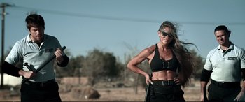 Movie still from “Debt Collectors” (2020), directed by Jesse V. Johnson – A woman in a black top and sunglasses posing for a picture; Medium shot, Low angle