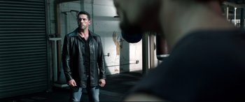 Movie still from “Debt Collectors” (2020), directed by Jesse V. Johnson – A man wearing a leather jacket standing next to a wall; Medium shot, Over the shoulder angle