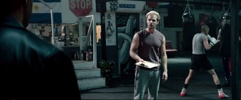 Movie still from “Debt Collectors” (2020), directed by Jesse V. Johnson – A man standing in front of a building holding a piece of paper; Medium shot, Over the shoulder angle