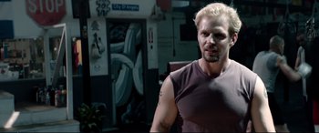 Movie still from “Debt Collectors” (2020), directed by Jesse V. Johnson – A man in a brown shirt is posing for a picture; Close Up shot, Over the shoulder angle