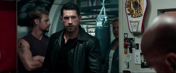 Movie still from “Debt Collectors” (2020), directed by Jesse V. Johnson – A man in a leather jacket standing in front of a punching bag; Medium shot, Over the shoulder angle